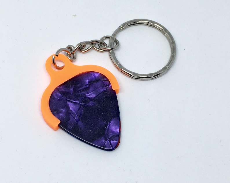 May include: A purple guitar pick keychain with an orange holder and a silver key ring.