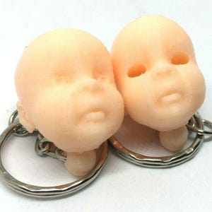 May include: Two small, realistic-looking baby doll heads attached to keychains. The dolls have light skin and are made of a smooth, soft material.