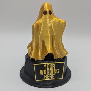 May include: A gold ghost trophy with a black base. The base has a plaque that says "YOUR WORDING HERE".