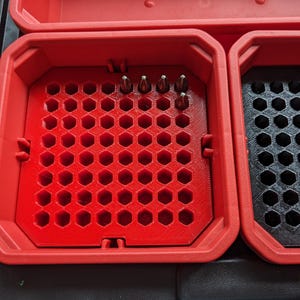 May include: A red plastic storage case with a honeycomb-shaped compartment for holding small items. The compartment has several small metal objects in it.