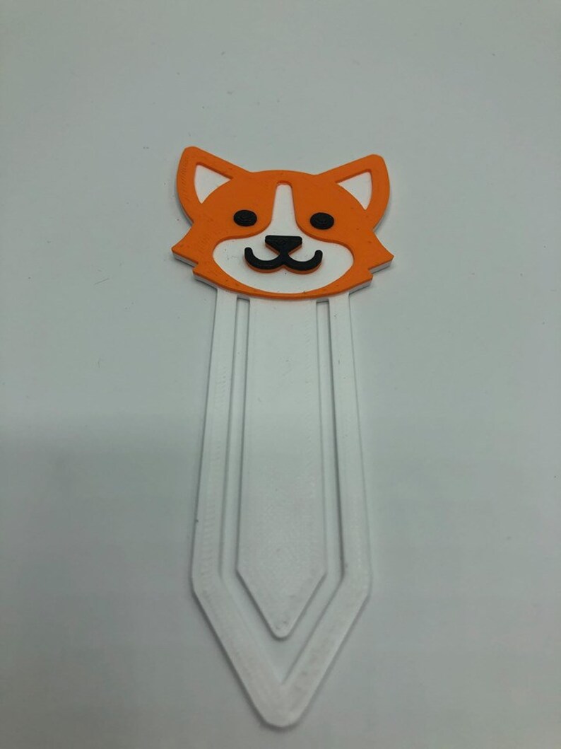 May include: Orange and white bookmark with a cartoon dog face. The bookmark has a white, three-pronged design.