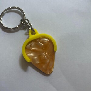 May include: A yellow guitar pick holder keychain with a brown and white guitar pick attached.