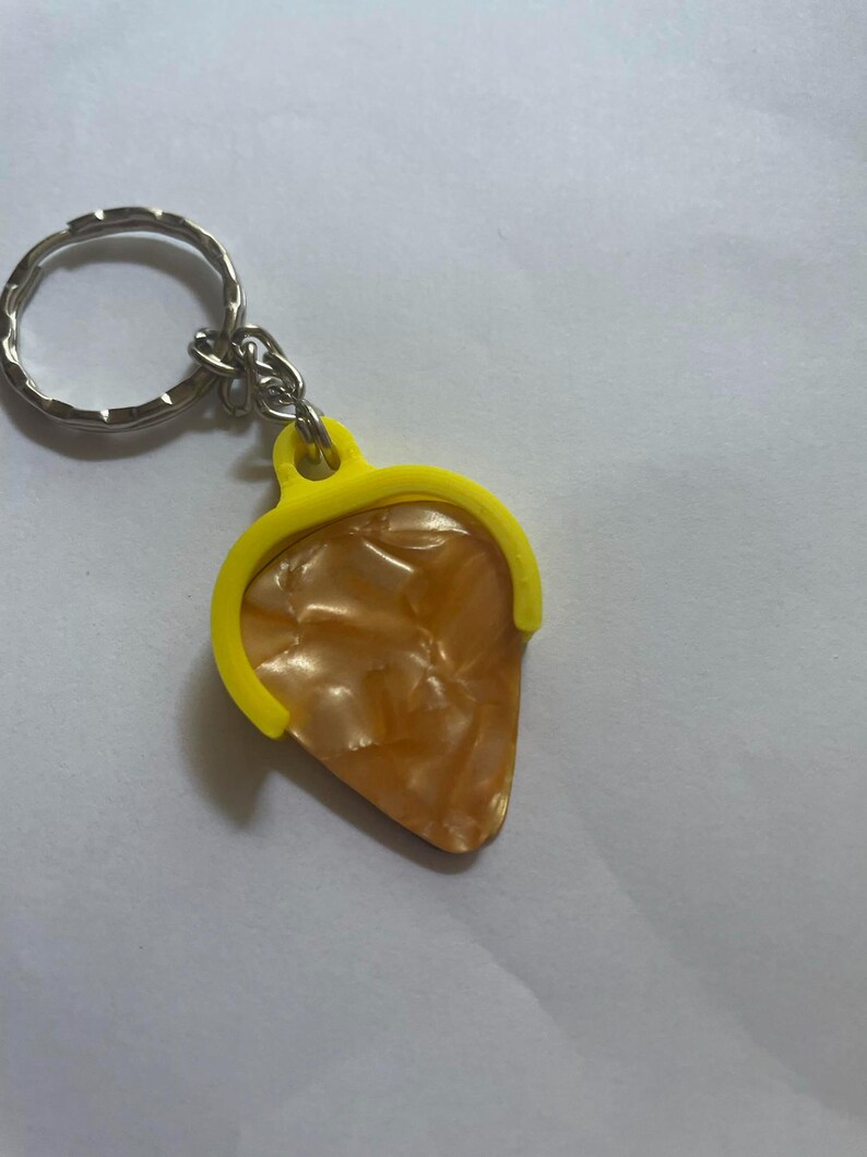 May include: A yellow guitar pick holder keychain with a brown and white guitar pick attached.