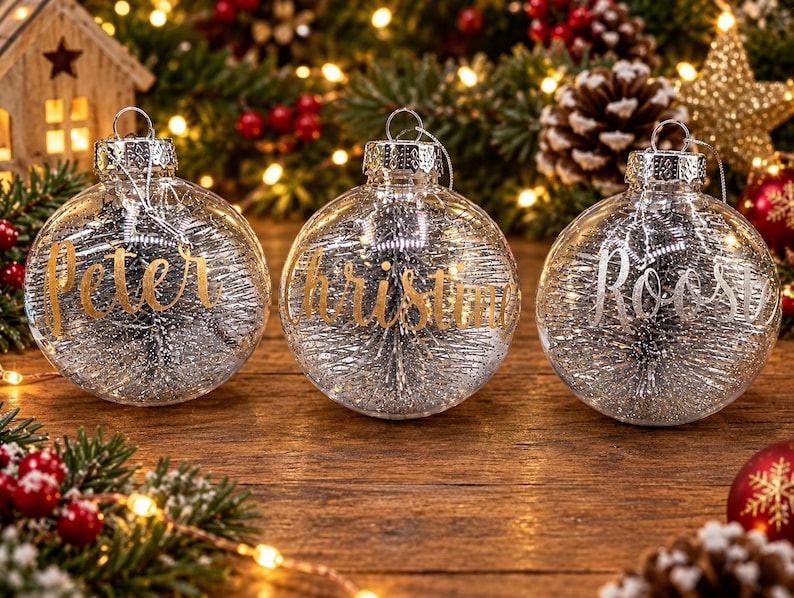 May include: Three clear spherical glass ornaments with silver tinsel filling. Each ornament features a name in cursive lettering: Peter and Christin in gold, and Roosy in silver. Each has a silver metal cap and a hanging loop.