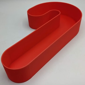 May include: A red candy cane shaped container made of plastic. The container is hollow and can be used to hold small items.