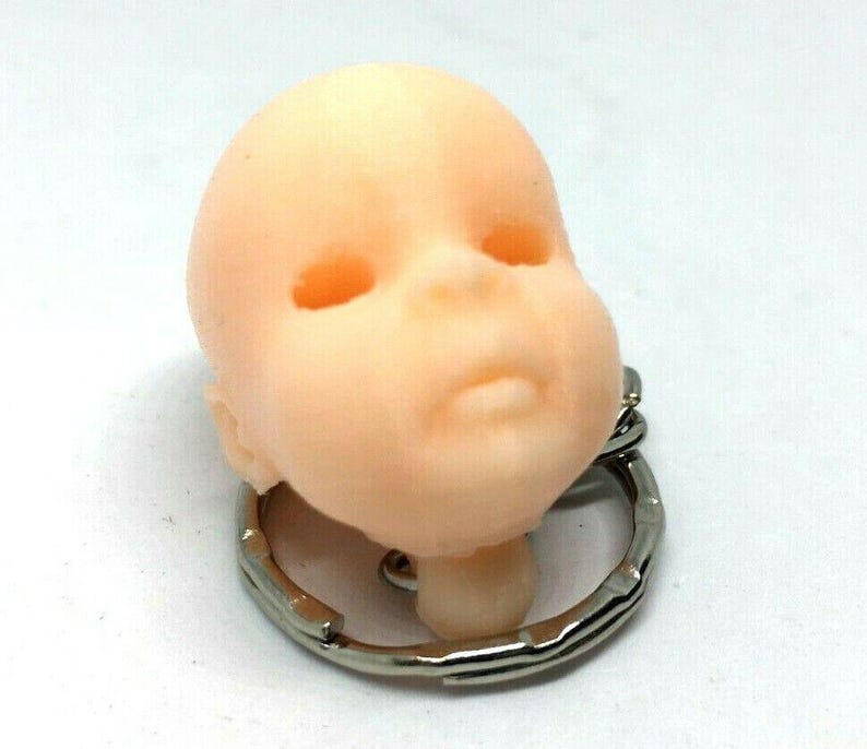 May include: A small, light pink baby doll head keychain with a silver metal key ring.