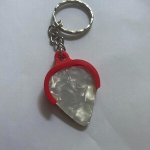 May include: A white guitar pick with a red plastic holder attached to a silver key chain.