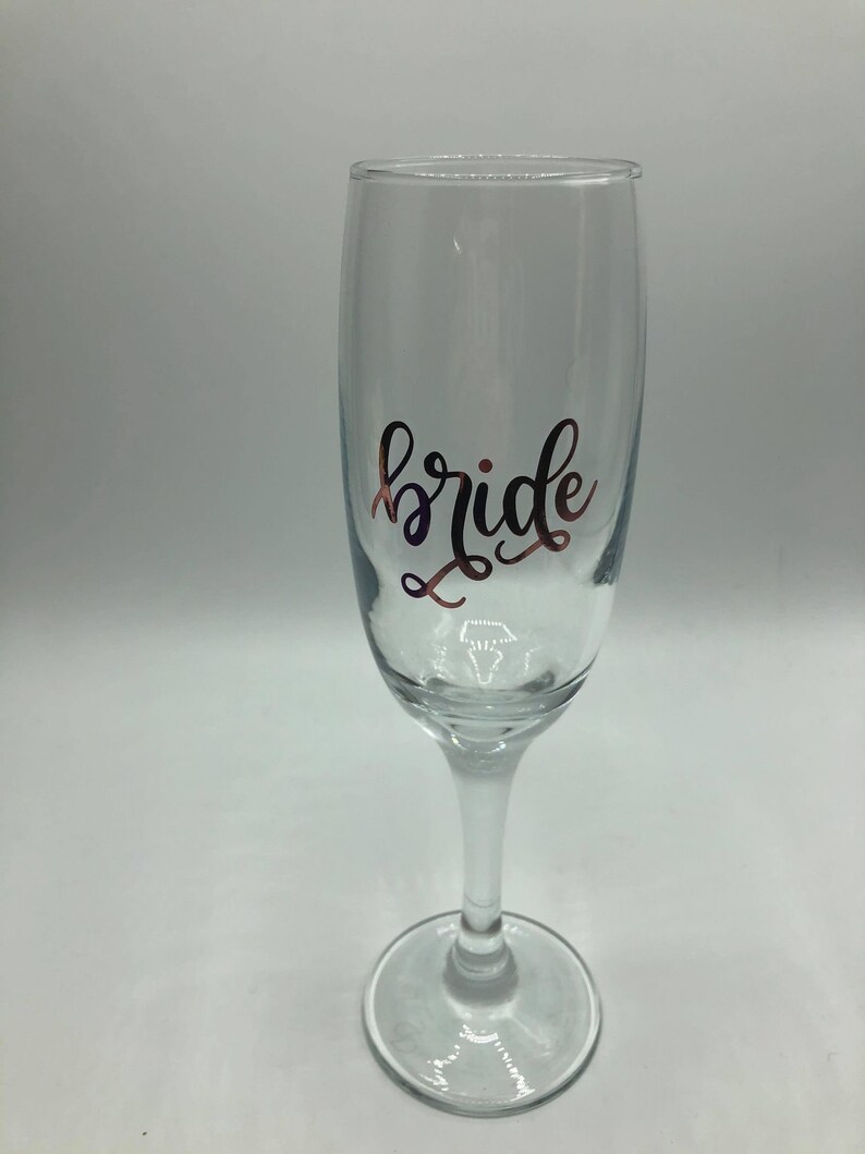 May include: A clear glass champagne flute with the word "bride" written in gold lettering.