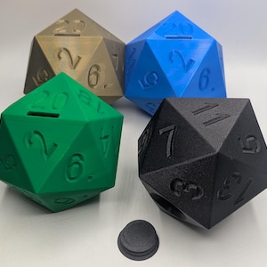 May include: Four 20-sided dice in different colors: green, blue, black, and gold. The dice are shaped like a dodecahedron and have numbers 1 through 20 printed on each face. The dice are sitting on a white surface.