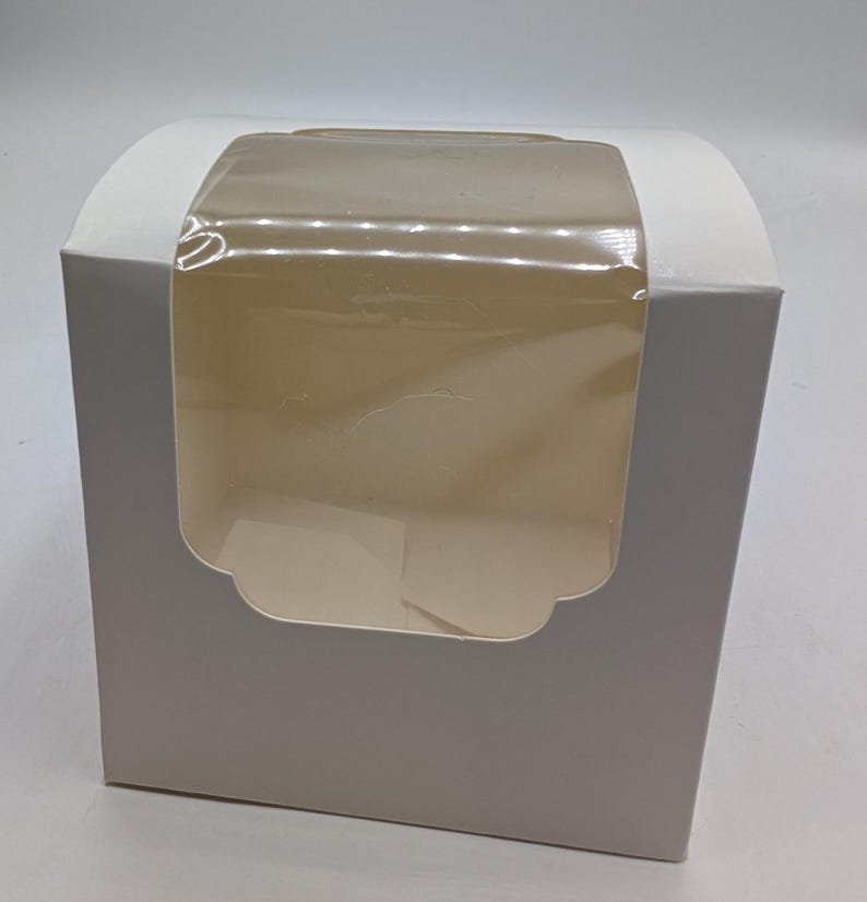 May include: A white cardboard box featuring a clear plastic window on the front panel. The box has a curved top design and a rectangular shape, providing a view into the interior space through the transparent film window.