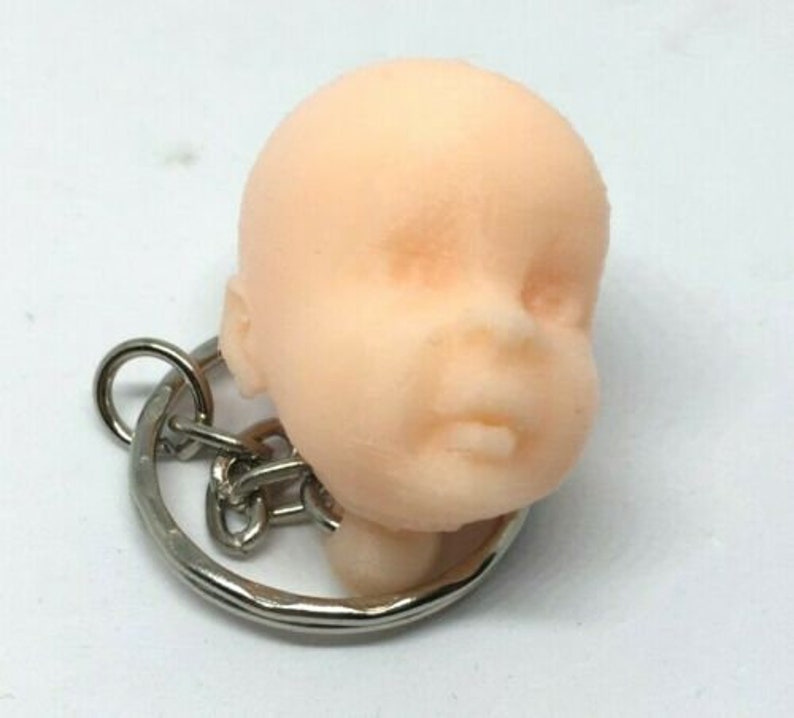 May include: A small, light pink, baby doll head keychain with a silver key ring.