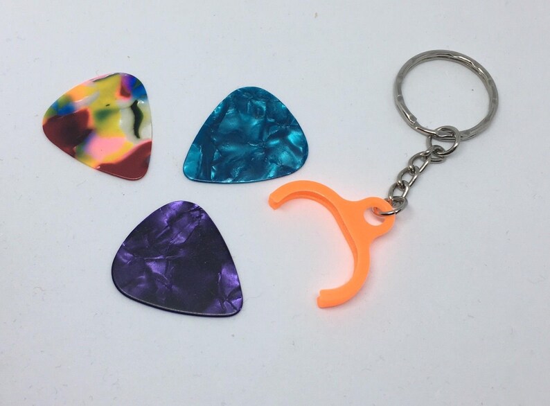 May include: Three guitar picks in different colors and patterns: multi-colored, blue, and purple. A keychain with an orange pick holder is also included.