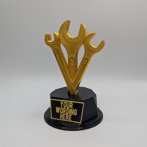 May include: A gold-colored trophy featuring three wrenches of varying sizes. The wrenches are mounted on a black base with a gold-bordered plaque that reads "YOUR WORDING HERE". The trophy is a unique award or gift.