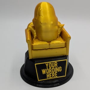 May include: A gold-coloured trophy featuring a person sitting on a sofa. The base of the trophy is black and has a plaque with the text "YOUR WORDING HERE".