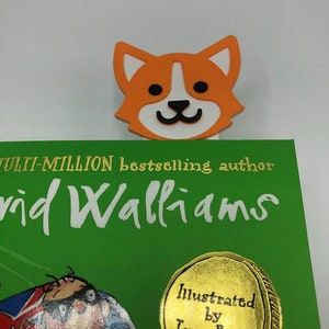 May include: An orange and white cartoon dog bookmark with a black nose and eyes. The bookmark is on top of a green book with the text "Multi-million bestselling author David Walliams" and a gold sticker that says "Illustrated by Tony Ross".