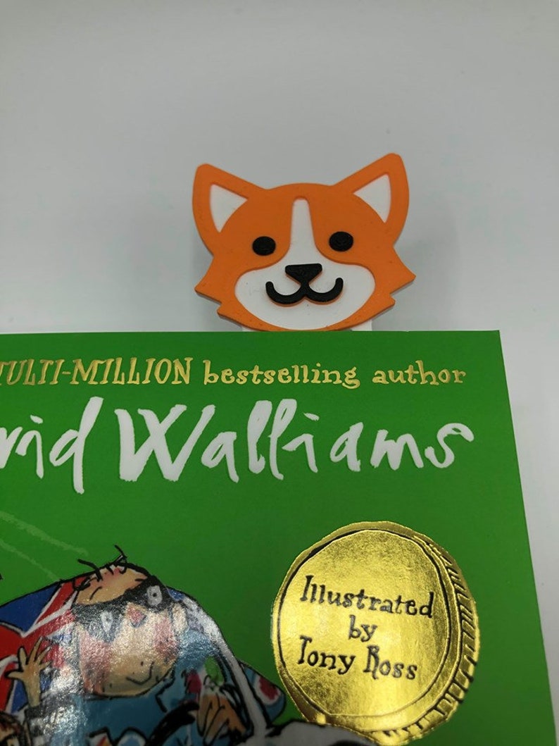 May include: An orange and white cartoon dog bookmark with a black nose and eyes. The bookmark is on top of a green book with the text "Multi-million bestselling author David Walliams" and a gold sticker that says "Illustrated by Tony Ross".