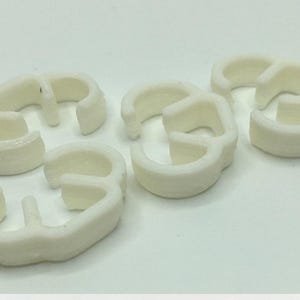 May include: Five white plastic cable ties with a unique three-loop design.