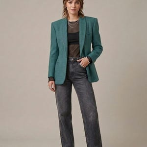 May include: A teal blazer with a small checkered pattern, worn over a black sheer long-sleeve top and a black camisole. The outfit includes charcoal gray straight-leg denim jeans with a raw hem and black chunky lug-sole loafers.