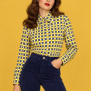 Pode incluir: Uma camisa de manga comprida com botões e um padrão geométrico repetitivo de círculos amarelos, brancos e pretos, combinada com calças de veludo cotelê azul-marinho de cintura alta. A camisa tem um colarinho clássico e uma carcela frontal.