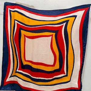 May include: A square scarf featuring a bold geometric pattern of concentric, wavy-edged squares in vibrant shades of navy blue, bright red, golden yellow, and crisp white, creating a dynamic, layered visual effect across the entire fabric surface.