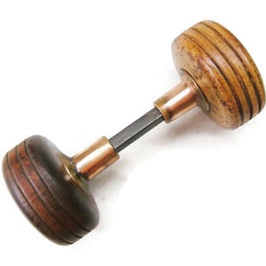 May include: A vintage wooden door knob with a dark brown finish and a copper-colored metal base. The knob has a ridged design and a square metal rod connecting the two sides. The hardware is set against a white background.