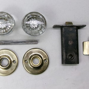 May include: An assortment of vintage door hardware, including two clear glass doorknobs, two brass-colored rosettes, a black metal latch, a brass-colored strike plate, and a connecting rod.