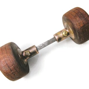 May include: A vintage door handle with two rounded wooden knobs connected by a metal rod. The knobs are a warm brown color, and the metal components have a brassy finish. The handle is designed for a door.
