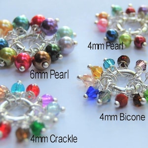 May include: Close-up of four different types of jewelry charms. The charms include 6mm pearls, 4mm pearls, 4mm crackle beads, and 4mm bicone beads. Each charm is attached to a silver-colored ring and features a variety of colorful beads.