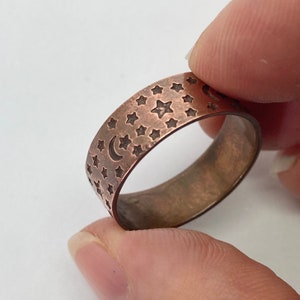 May include: A copper ring with a hammered finish and a design of stars and a crescent moon.