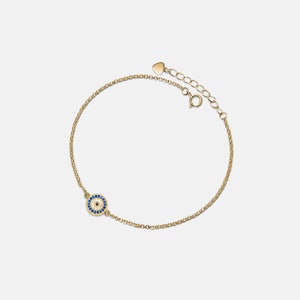 May include: A gold chain bracelet with a small blue and white evil eye charm. The bracelet has a heart-shaped clasp.