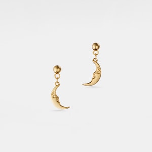 May include: A pair of gold crescent moon earrings with a face on the moon. The earrings are on a white background.