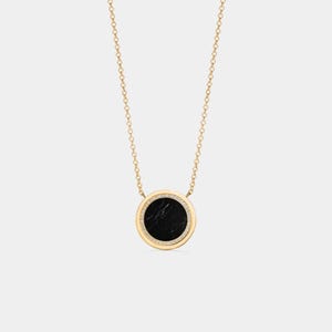May include: A gold-toned necklace featuring a circular pendant with a black stone center. The pendant is encircled by a row of small, clear stones. The necklace chain is delicate and gold-colored, creating an elegant and minimalist design.