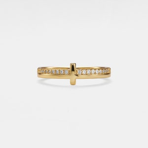 Puede incluir: Un anillo de oro con un pequeño diseño de cruz y una banda de pequeños diamantes.