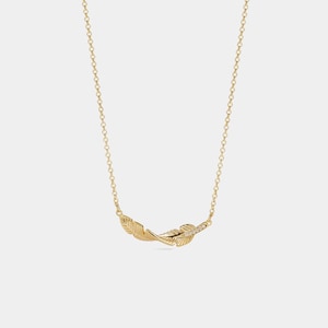 Puede incluir: Un collar dorado con dos colgantes de plumas estilizadas. Una pluma está adornada con pequeños adornos brillantes. La cadena del collar es delicada y está hecha de pequeños eslabones.