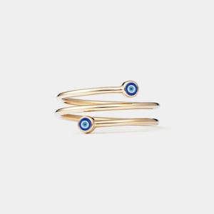 May include: Gold ring with three bands and two blue evil eye charms. The ring is a popular symbol of protection and good luck.