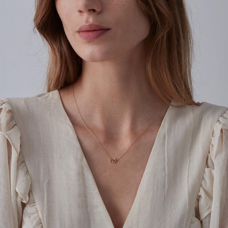 May include: A gold chain necklace with a small, delicate pendant made of multiple stacked rings.