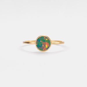 May include: A gold ring featuring a round opal gemstone. The opal displays a dark green, blue, and orange colour.
