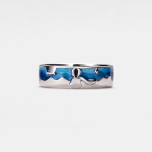 May include: A silver ring featuring a blue enamel design of a mountain range and stars. The ring is a wide band with a raised design.