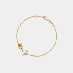 Peut inclure: Un bracelet en or délicat avec un motif de tulipe. La tulipe a un centre jaune-orangé et est ornée de petites pierres scintillantes sur la tige. Le bracelet est une fine chaîne avec une fermeture à fermoir.
