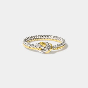 Puede incluir: Un anillo de plata y oro con un diseño anudado. El anillo está hecho de dos hebras de metal entrelazadas, una de plata y otra de oro.