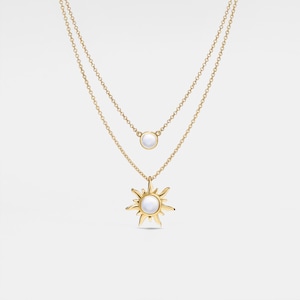 Può includere: Una collana dorata a due fili con un ciondolo a forma di sole e un piccolo ciondolo a forma di perla. Il ciondolo a forma di sole ha un centro di perla e un design a stella.