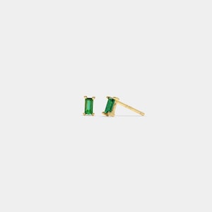 May include: A pair of gold stud earrings, each with a rectangular, emerald-green gemstone. The earrings have a simple, minimalist design, suitable for daily wear. The gold has a polished finish, reflecting light.