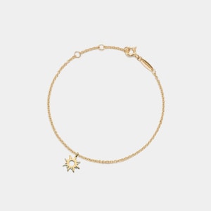 May include: A gold chain bracelet featuring a small sun charm. The chain is delicate and the sun charm is simple and elegant.
