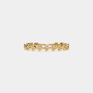 May include: A gold-colored ring featuring a repeating leaf design. The ring is thin and delicate, with the leaves arranged in a continuous pattern around the band. The ring is set against a plain white background.