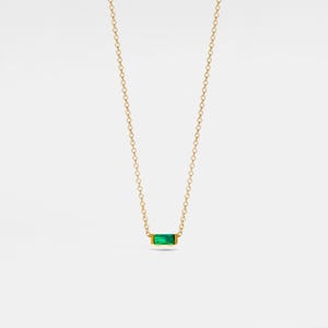May include: A delicate gold chain necklace with a small, rectangular emerald green gemstone pendant.