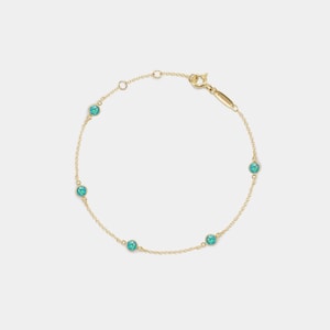 May include: A delicate gold chain bracelet featuring five round, turquoise-colored gemstones. The bracelet has a simple design with a lobster clasp closure. The gemstones are evenly spaced along the chain, creating a subtle sparkle.