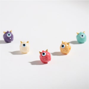 May include: Five small, colorful, plastic figurines with a single eye and horns. The figurines are in various colors, including purple, white, pink, yellow, and blue.
