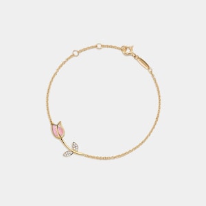 Puede incluir: Un delicado brazalete de cadena dorada con un dije de tulipán rosa adornado con pequeños diamantes.