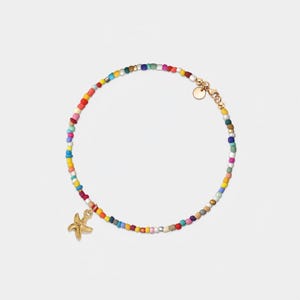 May include: A colorful beaded bracelet with a gold starfish charm. The bracelet is made of small, round beads in various colors, including red, orange, yellow, green, blue, purple, and white. The beads are strung on a thin gold chain.