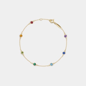 May include: A fine gold bracelet with seven colourful gemstones. The gemstones are red, orange, green, blue, purple, and two shades of blue. The bracelet has a delicate chain and a clasp closure.
